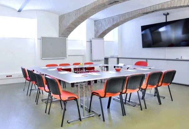 Leerer Seminarraum mit Tischinsel, roten Stühlen und Bildschirm