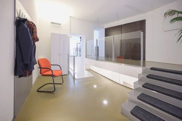 Garderobe mit Jacken und rotem Stuhl, dahinter die Treppe ins Institut